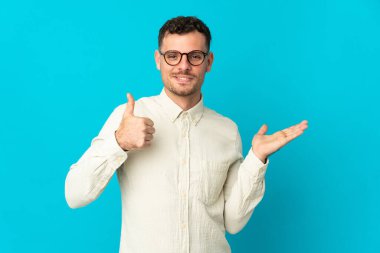 Beyaz tenli yakışıklı adam mavi arka planda izole edilmiş. Kopyalama alanı hayali bir şekilde avucunun içinde duruyor. Bir ilan vermek için.