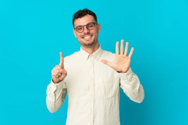 Beyaz tenli yakışıklı adam mavi arka planda izole edilmiş. Parmakları olan altı kişi saydım.