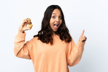 Soyutlanmış beyaz arka plan üzerinde genç bir kadın renkli Fransız badem kurabiyeleri tutuyor ve harika bir fikri işaret ediyor.