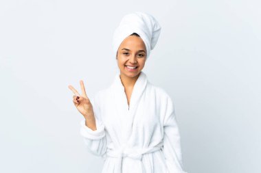 Bornozlu genç kadın izole edilmiş beyaz arka planda gülümsüyor ve zafer işareti gösteriyor.