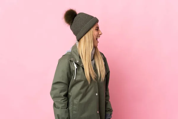 年轻女子头戴冬帽 背靠粉色背景 侧身笑着 — 图库照片