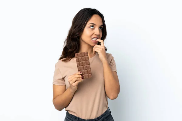 Mladá Žena Izolovaném Bílém Pozadí Čokoládovou Tabletu Mají Pochybnosti — Stock fotografie