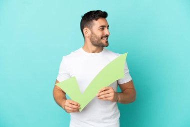 Mavi arka planda izole edilmiş yakışıklı, beyaz bir adam elinde bir çek simgesi, diğer tarafa bakıyor.