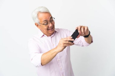 Orta yaşlı Brezilyalı adam beyaz arka planda izole edilmiş cep telefonuyla oynuyor.