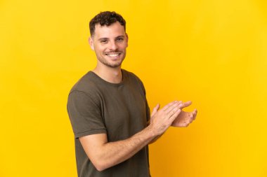 Sarı arka planda izole edilmiş beyaz, yakışıklı bir adam alkışlıyor.