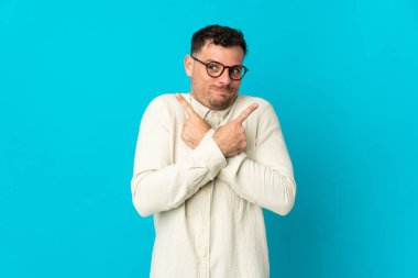 Mavi arka planda soyutlanmış beyaz, yakışıklı genç bir adam. Yan taraftakilerin şüphelerini gösteriyor.