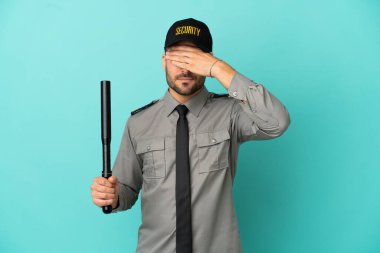 Genç güvenlik görevlisi mavi arka planda tek başına, gözleri elle kapatıyor. Bir şey görmek istemiyorum.