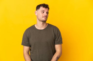Sarı arka planda izole edilmiş beyaz, yakışıklı genç bir adam şüpheli hareketler yapıyor.