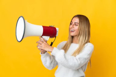 Sarı arka planda izole edilmiş genç sarışın bir kadın megafondan bir şey duyurmak için bağırıyor.