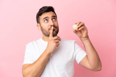 Elinde pembe arka planda izole edilmiş Bitcoin tutan genç bir adam.