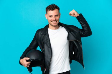 Mavi arka planda izole edilmiş motosiklet kasklı beyaz adam güçlü bir jest yapıyor.