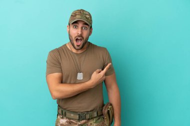 Mavi arka planda izole edilmiş künyeli ordu. Şaşırmış ve işaret ediyor.