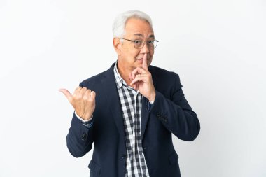 Beyaz arka planda izole edilmiş orta yaşlı Brezilyalı bir adam, yan tarafı işaret ediyor ve sessizlik jesti yapıyor.