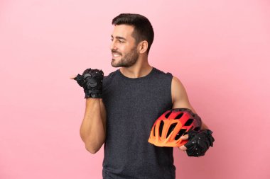 Pembe arka planda izole edilmiş genç bisikletçi bir ürünü sunmak için kenarı işaret ediyor.