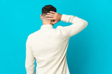 Kafkasyalı yakışıklı genç adam mavi arka planda izole edilmiş ve düşünüyor.