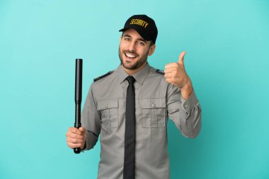 Genç güvenlik görevlisi mavi arka planda izole edildi. Başparmakları havada çünkü iyi bir şey oldu.