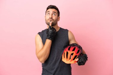 Pembe arka planda izole edilmiş genç bisikletçi yukarı bakarken şüpheleri var.