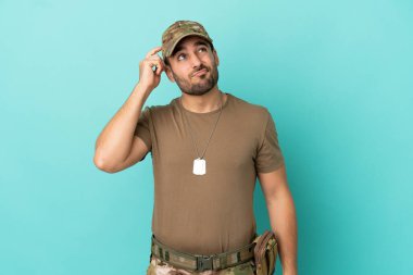 Mavi arka planda izole edilmiş künyeli ordu kuşkuları ve kafa karıştırıcı yüz ifadesiyle