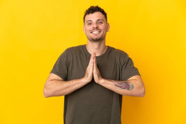 Sarı arka planda izole edilmiş beyaz, yakışıklı genç bir adam avuç içlerini bir arada tutuyor. İnsan bir şey ister.