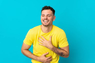 Beyaz tenli yakışıklı bir adam mavi arka planda izole edilmiş, gülümsüyor.