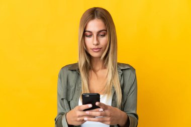 Sarı arka planda cep telefonu kullanan genç sarışın kadın.