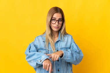 Sarı arka planda izole edilmiş genç sarışın kadın geç kalma jesti yapıyor.