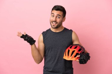 Pembe arka planda izole edilmiş genç bisikletçi, davet edilmek için ellerini yana uzatıyor.