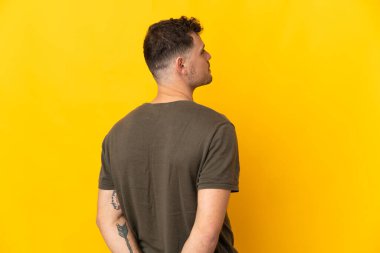 Beyaz tenli yakışıklı adam sarı arka planda izole edilmiş ve arkasına bakıyor.