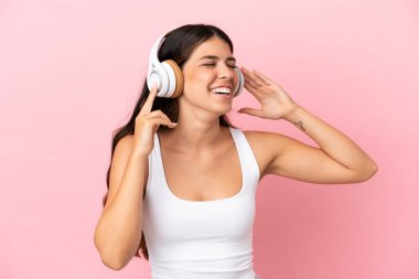 Genç beyaz kadın pembe arka planda izole edilmiş müzik dinliyor ve şarkı söylüyor.