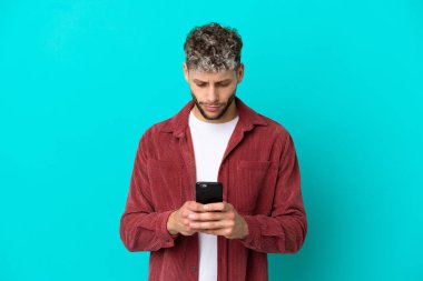 Genç yakışıklı beyaz adam mavi arka planda cep telefonu kullanarak izole edilmiş.