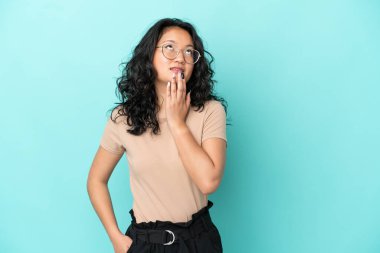 Genç Asyalı kadın mavi arka planda izole edilmiş gülümserken yukarı bakıyor.