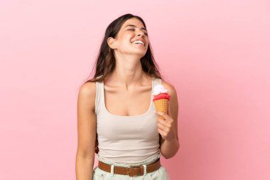 Pembe arka planda izole edilmiş kornet dondurmalı beyaz bir kadın gülüyor.