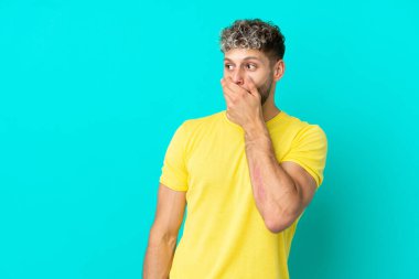 Genç, beyaz, mavi arka planda izole edilmiş bir adam. Yan tarafa bakarken sürpriz jest yapıyor.