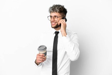 Beyaz arka planda izole edilmiş beyaz bir iş adamı elinde kahve ve bir cep telefonu tutuyor.