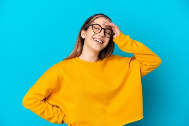 Mavi arka planda izole edilmiş genç beyaz kadın çok gülümsüyor.