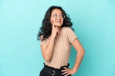 Genç Asyalı kadın mavi arka planda izole edilmiş bir şekilde bakarken bir fikir düşünüyor.