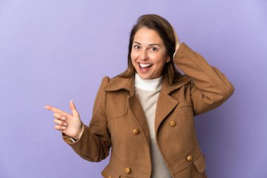 Mor arka planda izole edilmiş orta yaşlı Brezilyalı kadın şaşırmış ve parmağıyla kenarı işaret ediyor.