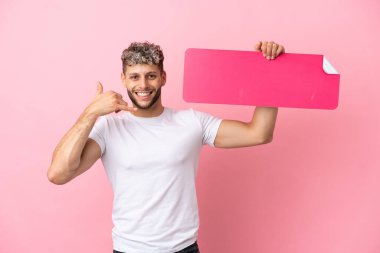 Pembe arka planda izole edilmiş yakışıklı beyaz bir adam boş bir levha tutuyor ve telefon hareketi yapıyor.