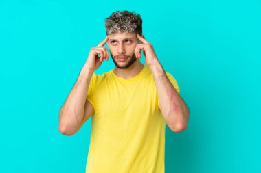 Mavi arka planda soyutlanmış yakışıklı, beyaz bir adam. Şüpheleri ve düşünceleri var.