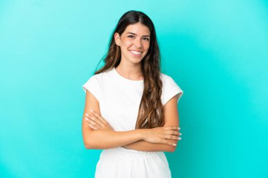 Mavi arka planda izole genç beyaz kadın kollarını ön cephede çapraz tutuyor.