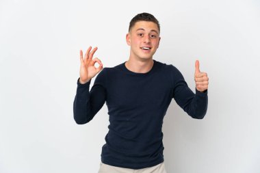 Beyaz arka planda izole edilmiş genç beyaz bir adam Tamam işareti ve baş parmak işareti