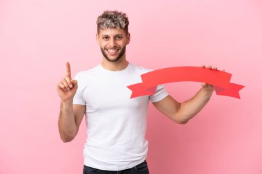 Pembe arka planda izole edilmiş yakışıklı beyaz bir adam boş bir levha tutuyor ve yukarı bakıyor.