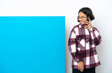 Beyaz arka planda izole edilmiş büyük mavi pankartlı melez bir kadın cep telefonuyla sohbet ediyor.