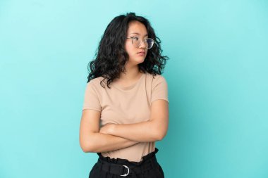 Mavi arka planda izole edilmiş genç Asyalı kadın kollarını çapraz tutuyor.