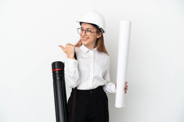 Miğferli ve elinde beyaz arka planda izole edilmiş planları olan genç bir mimar kadın bir ürünü sunmak için kenarı işaret ediyor.