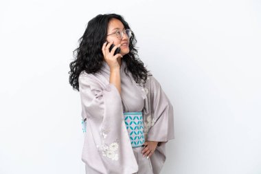 Beyaz arka planda kimono giyen genç Asyalı bir kadın cep telefonuyla sohbet ediyor.