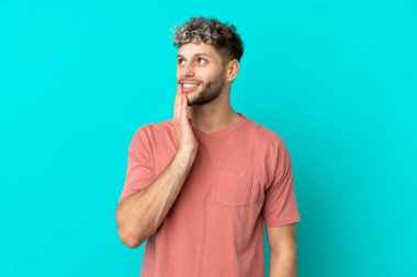 Mavi arka planda izole edilmiş yakışıklı beyaz adam gülümserken yukarı bakıyor.