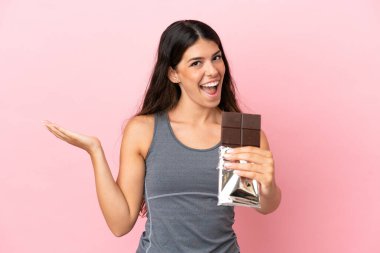 Pembe arka planda izole edilmiş beyaz bir kadın çikolata tableti alıyor ve şaşırıyor.