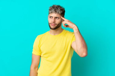 Genç, beyaz, mavi arka planda izole edilmiş bir adam deliliğin jestini yapıyor. Parmağını kafaya koyuyor.