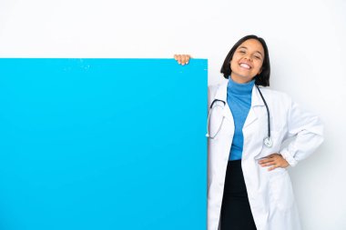 Beyaz arka planda izole edilmiş, kalçasında kollarıyla poz veren ve gülümseyen büyük bir afişi olan genç ırk doktoru kadın.
